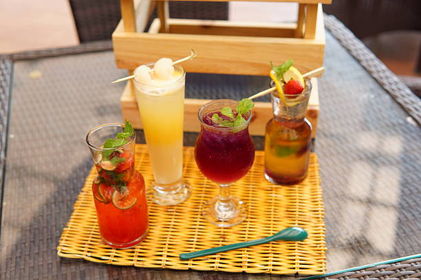 Variety of vibrant, refreshing cold beverages garnished with fresh fruits and mint, served on a textured woven placemat on an outdoor patio table