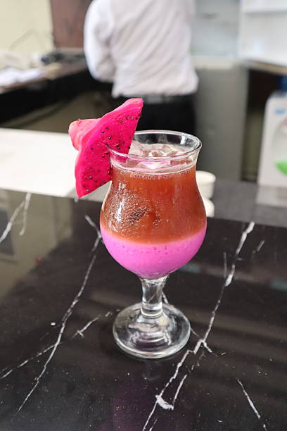 A vibrant two layered smoothie, pink and reddish brown, is served in a glass goblet with ice Its elegantly garnished with a fresh slice of bright pink dragon fruit
