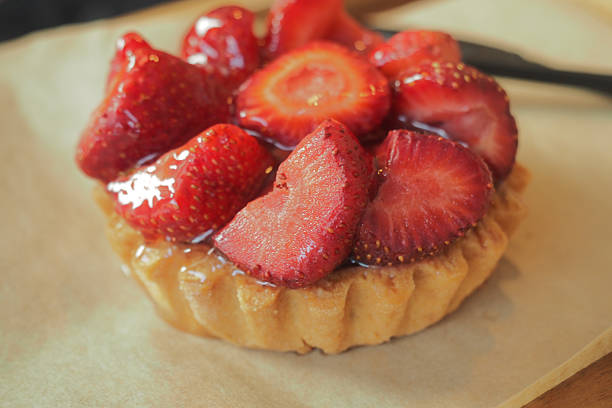 A delicious strawberry tart sits on a wooden board, showcasing fresh berries.
