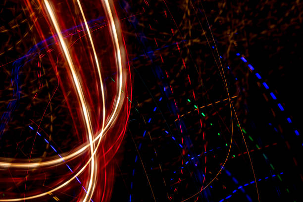 Bright light trails and spots create futuristic patterns against a dark backdrop. Abstract background with glowing curves and spots, made by glowing fiber optic lights.
