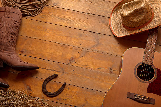 Acoustic guitar, rope, old horseshoe, cowboy hat and boots on a barn wood texture background. American Country music concept. Space for copy.