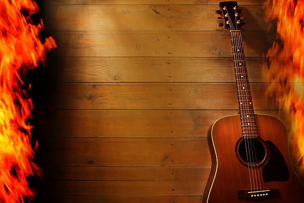 A guitar leans on a wooden wall while flames rise on either side. The warm light creates a dramatic atmosphere. The scene conveys a sense of energy and music. Space for copy.