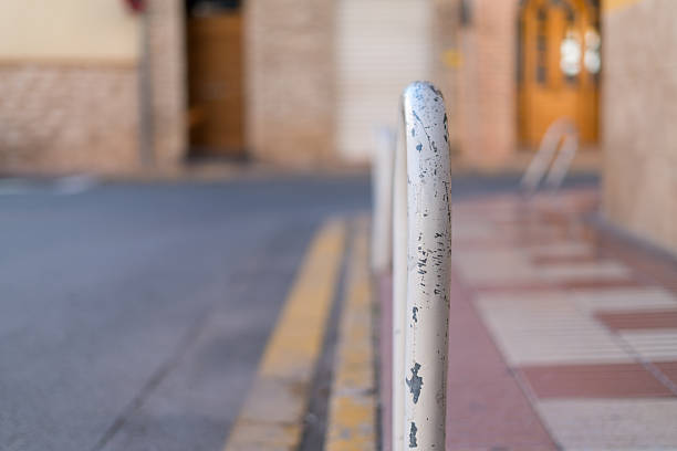 Close up of white metal street bollard on sidewalk with shallow depth of field and blurred city background. Urban detail with copy space.