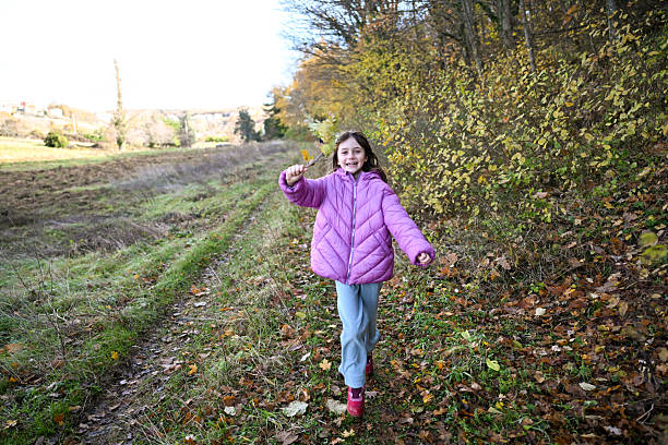 Young girl smiling, running on a path through an autumn forest, holding colorful leaves