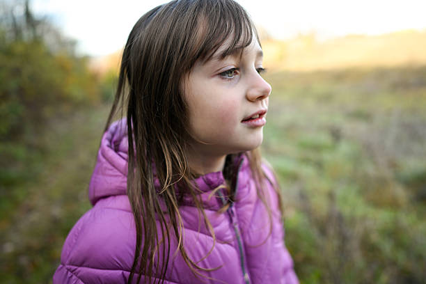 Child wearing a purple jacket looking away with a thoughtful expression outdoors