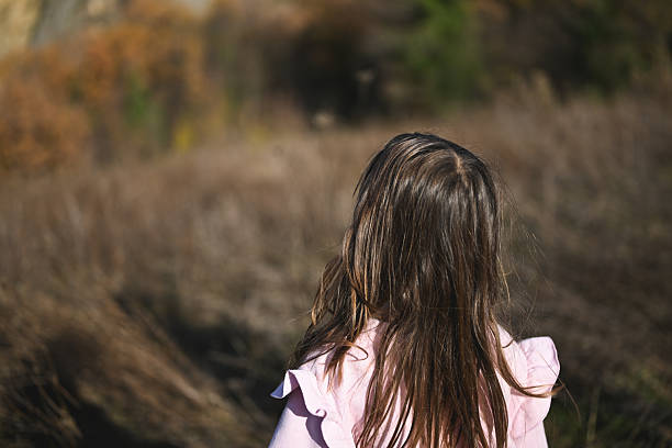 Child standing in a dry field, looking away towards the horizon with brown hair