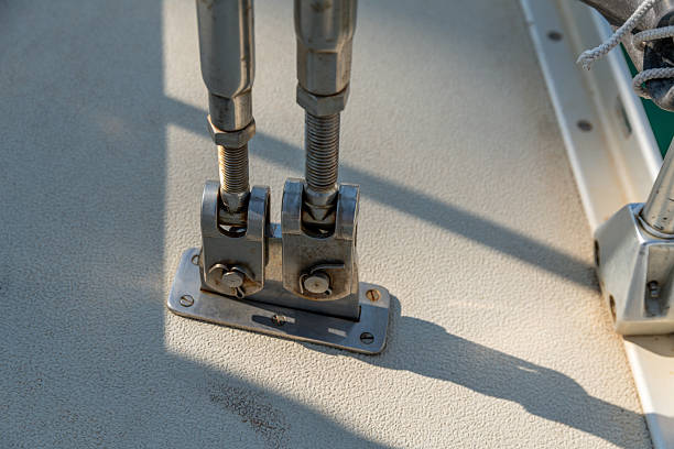 Close-up of two stainless steel turnbuckles secured on a sailboat deck, showing detailed rigging hardware with shadows on textured surface.