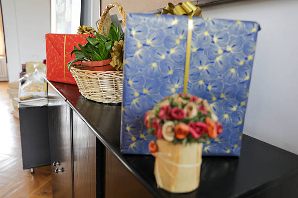 Festive Gift Boxes And Decorative Floral Arrangement Displayed On A Cabinet, Creating A Cozy Holiday Interior With Wrapped Presents, Natural Light, And Seasonal Home Decor.