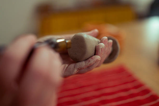 Close-up shot focused on the dusty hands of an artisan applying pressure to the base or interior of a small, hand-built clay object
