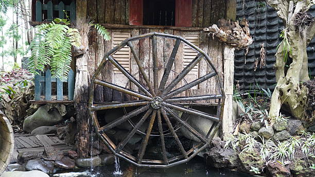 Explore this picturesque scene featuring a rustic water wheel nestled against a weathered wooden structure surrounded by lush greenery and natural elements providing a serene landscape