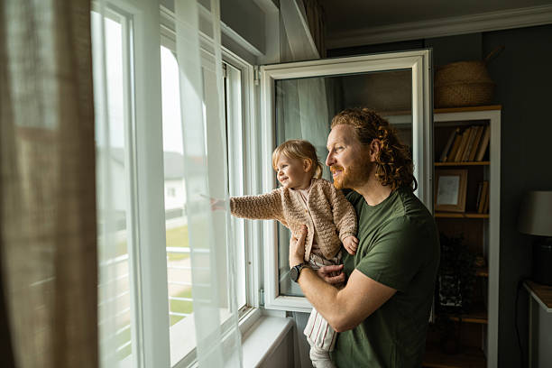 Father holding his child, looking outside through window at their house