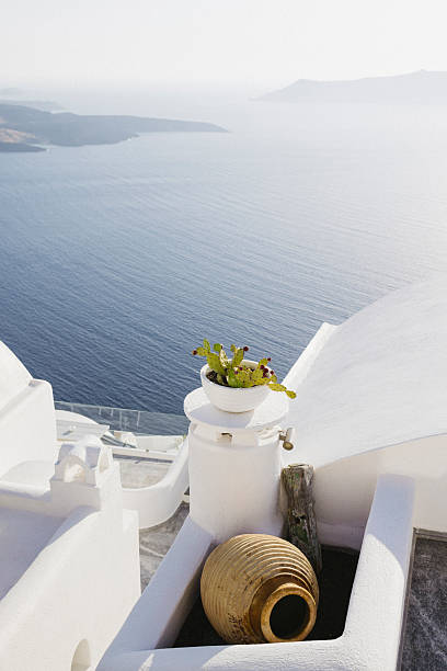 Vertical view of a terracotta vase lying on its side in the foreground with whitewashed buildings and the turquoise Aegean Sea in the background, Santorini, Greece. Mediterranean lifestyle scene.