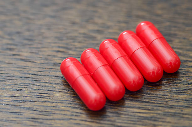 Five Red Capsules Aligned Diagonally on Dark Wooden Surface Representing Medication and Pharmaceutical Concept