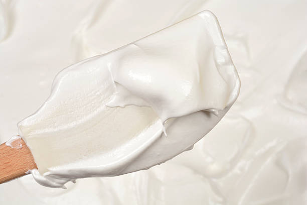 Close up of a wooden spatula lifting a glossy thick mixture of whipped egg whites and sugar during the process of preparing meringue layers