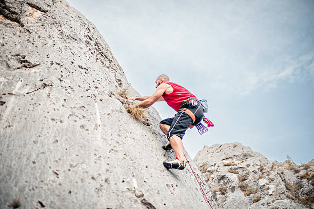 An adaptive climbing student pauses midway through an ascent, gripping the rope system while catching their breath before continuing. The image captures the tension, control, and quiet determination in moments of physical challenge—highlighting resilience, self-awareness, and strategic recovery in sport.