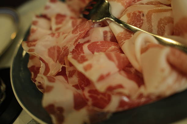 A detailed close-up of a variety of authentic Italian cured meats. A stainless steel fork rests on top of the thinly sliced salumi, highlighting the texture and freshness of the appetizer.