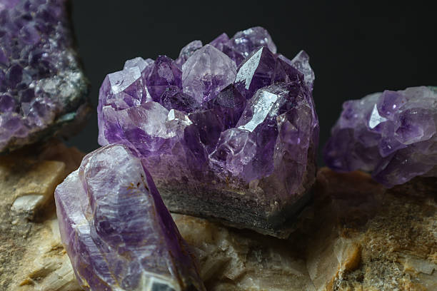 Close-up of hands holding a raw amethyst crystal. The hands are adorned with bracelets, and the background is softly blurred, emphasizing the crystal's intricate details and colors.