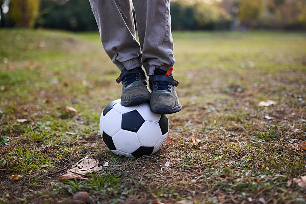 Low Section Of Child Playing Soccer On Grass