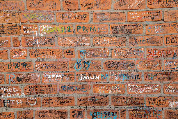 Izmir, Turkey - Close-up view of a textured red brick wall covered with handwritten names, dates, drawings and colorful graffiti made by visitors, reflecting urban culture, personal memories and spontaneous street art in a popular historic area of Izmir, creating a raw background with strong texture and visual detail