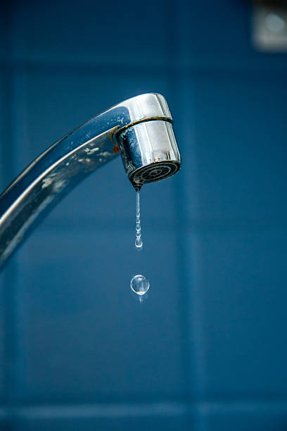 Leaky faucet dripping water against blue tiled background