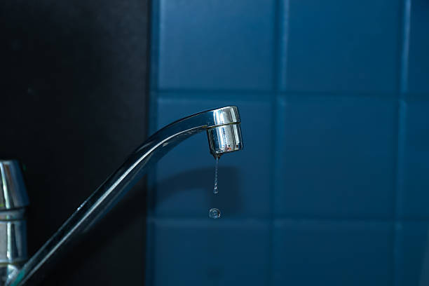 Leaking faucet dripping water against blue tile background