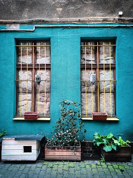 Facade of an old building with turquoise walls, yellow window bars, and flower boxes. Urban architecture with colorful details.