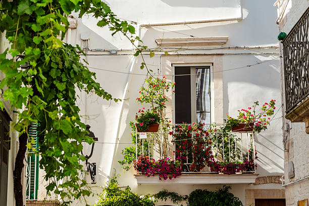 Taormina, Sicily, Italy - July 5, 2024: Historic downtown. Flowers and plants on yellow apartment facade balconies and roof. Green shuttered windows