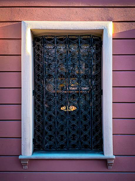 Elegant window with a decorative black wrought iron grill on a pink wall, architectural detail with soft evening light.