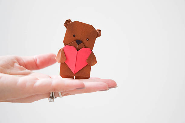 Woman’s hand holding an origami bear with a paper heart, Valentine’s Day love concept