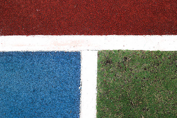 Abstract composition of modern sports flooring showing a three way intersection of red track surface, blue rubber flooring, and green grass. White marking lines clearly divide each zone, emphasizing geometry, movement, and functional athletic design. Ideal for sports branding, architectural concepts, digital backgrounds, and creative commercial projects.