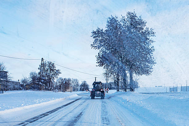 snow removal tractor drives ahead of a car.