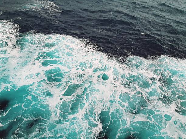 High-angle view of white sea foam and turquoise bubbles created by a ship's wake in the deep blue waters of the North Sea near Norway.