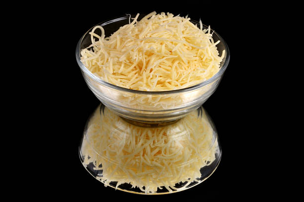 Closeup of a ramekin of grated cheese isolated on a black background with its reflection