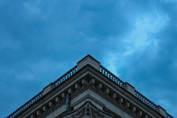Low-angle view of a historical building's roof with decorative moldings and a classic stone balustrade, set against an intense moody blue sky
