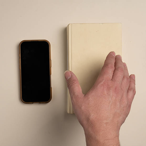 Hand choosing a book instead of a smartphone on neutral background, representing digital balance, mindful habits and preference for offline focus in everyday life.