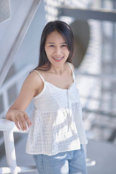 A young woman exudes joy and confidence while posing in a bright, modern space illuminated by natural light. Her relaxed posture and casual attire create an inviting atmosphere.