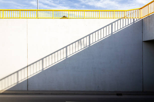 Yellow bridge railing and a shadow of it on concrete wall. Architectural detail.