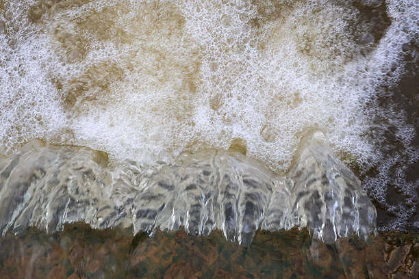 Top view of water rushing over a rocky ledge creating white foam and bubbles in a natural stream or river.