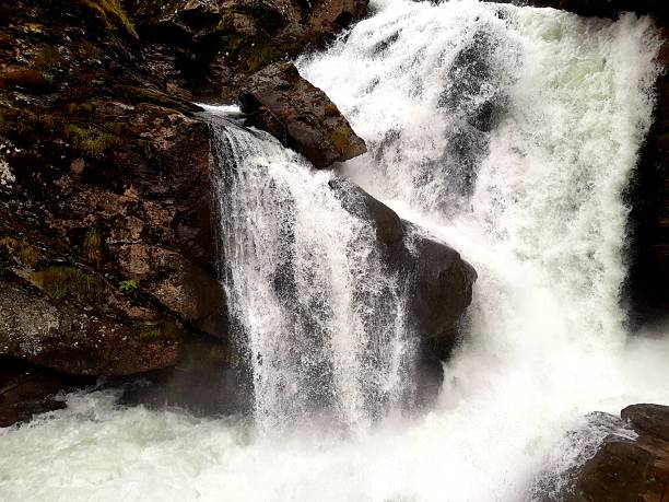 A detailed view of a heavy waterfall split by dark, mossy boulders, capturing the raw power of nature in the Geiranger district.