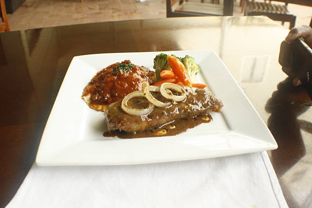 Savory steak dinner served on a white rectangular plate, accompanied by mashed potatoes with a rich sauce, tender broccoli, and sweet carrots
