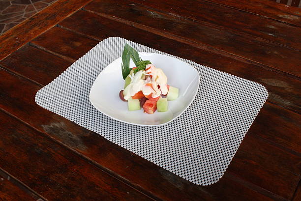 Delicious mixed fruit salad featuring watermelon, honeydew, and grapes with a creamy dressing, served on a white plate atop a dark wooden table