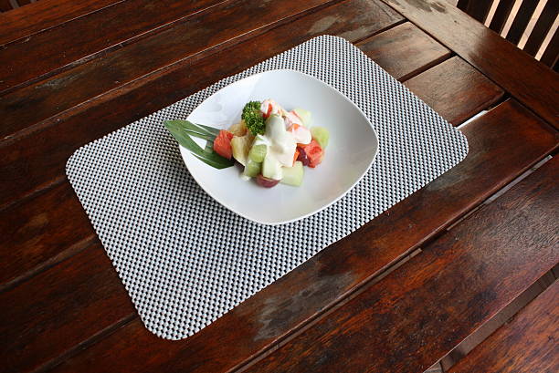 Colorful fruit salad featuring watermelon, melon, and grapes, topped with creamy dressing and green garnish, served on a rustic wooden table