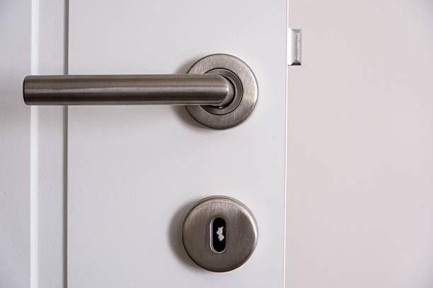 Close-up of a contemporary stainless steel door handle with lock cylinder on a white interior door. Minimalist home security and modern interior design concept with copy space.