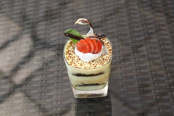 Beautiful layered dessert served in a glass, garnished with fresh sliced strawberries, a mint leaf, and delicate chocolate curls, dusted with cocoa powder