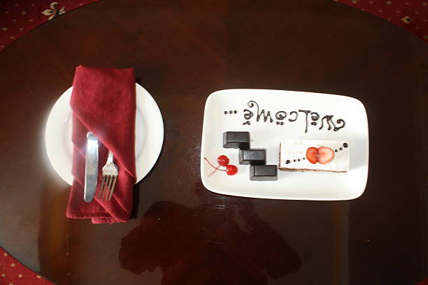 Plate with Welcome message, chocolate squares, strawberry cake, and cherries, thoughtfully presented on a dark wood table alongside a formal place setting