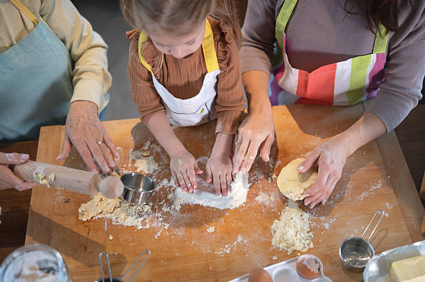 Close-up of a multigenerational family baking together at home, hands shaping cookie dough with a child, sharing joy, learning, and warm moments in a cozy kitchen