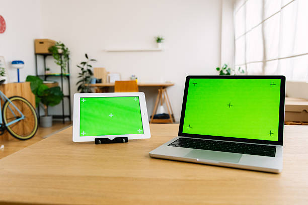 Modern laptop and digital tablet displaying green screens on a wooden desk, representing technology, remote work, mockups, and digital content creation in an contemporary workspace
