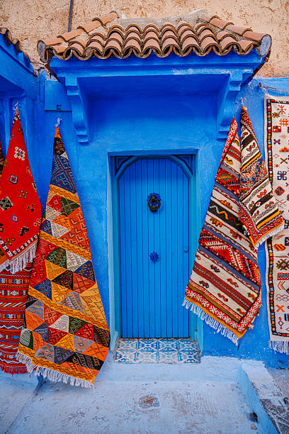 Vivid blue doorway framed by traditional Moroccan textiles in Chefchaouen. The striking color palette, geometric patterns, and inviting doorway evoke travel, culture, and craft in a charming street scene.