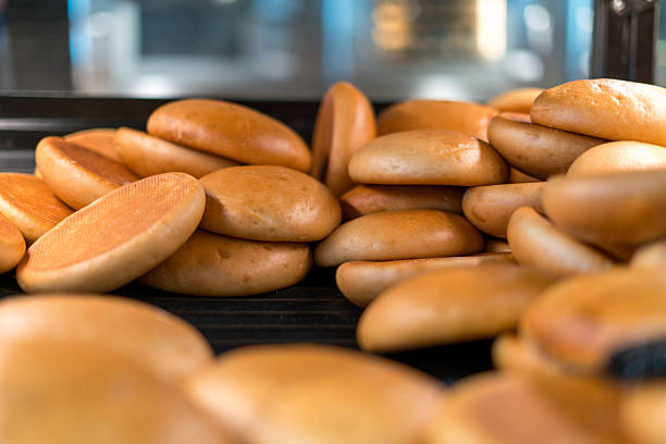 Freshly baked burger buns on bakery conveyor or rack industrial bread production food factory process baking and fast food ingredients concept
