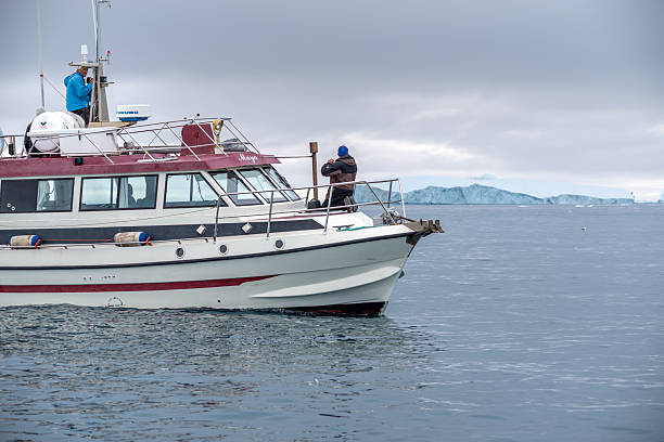 August 11, 2022 - Ilulissat, Greenland: Tourists sailing on an expedition boat, exploring icy arctic waters and viewing massive icebergs near Ilulissat, Greenland, experiencing remote travel and adventure in nature